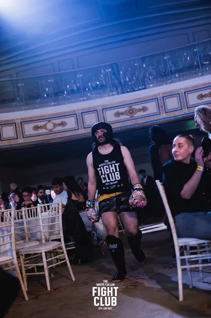 Alex walking out to the ring at a White Collar Fight Club event in London, wearing headgear and gloves.